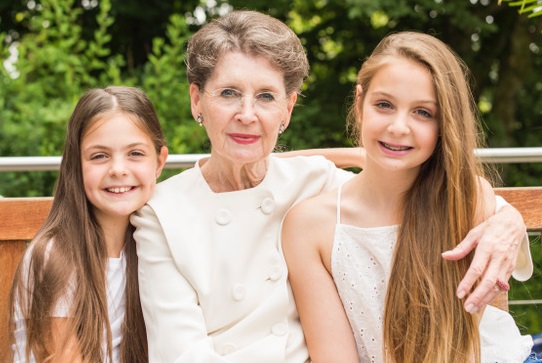 Renate Huch mit ihren zwei Enkelinnen auf einer Bank im Grünen sitzend